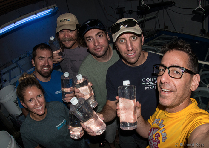 Happy people holding bottles containing thousands of swimming baby corals. Photo by Rich Ross.